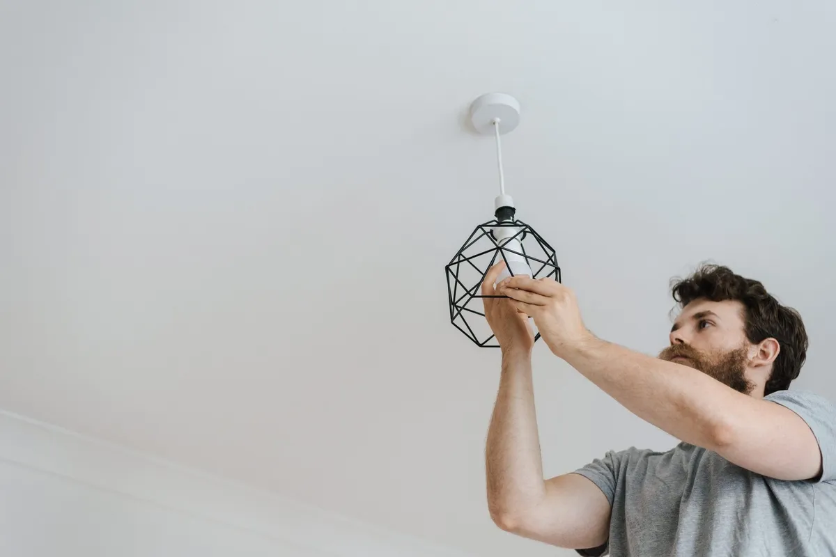 A man screws a light bulb into a stylish lamp during apartment renovation, highlighting DIY electrical work.